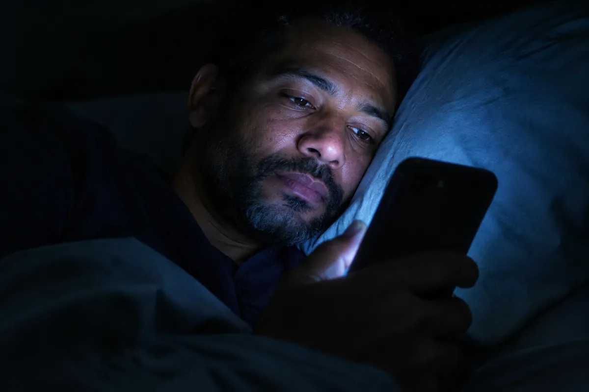 A man lying in bed at night, his face lit by his phone screen as he reads a calming message.